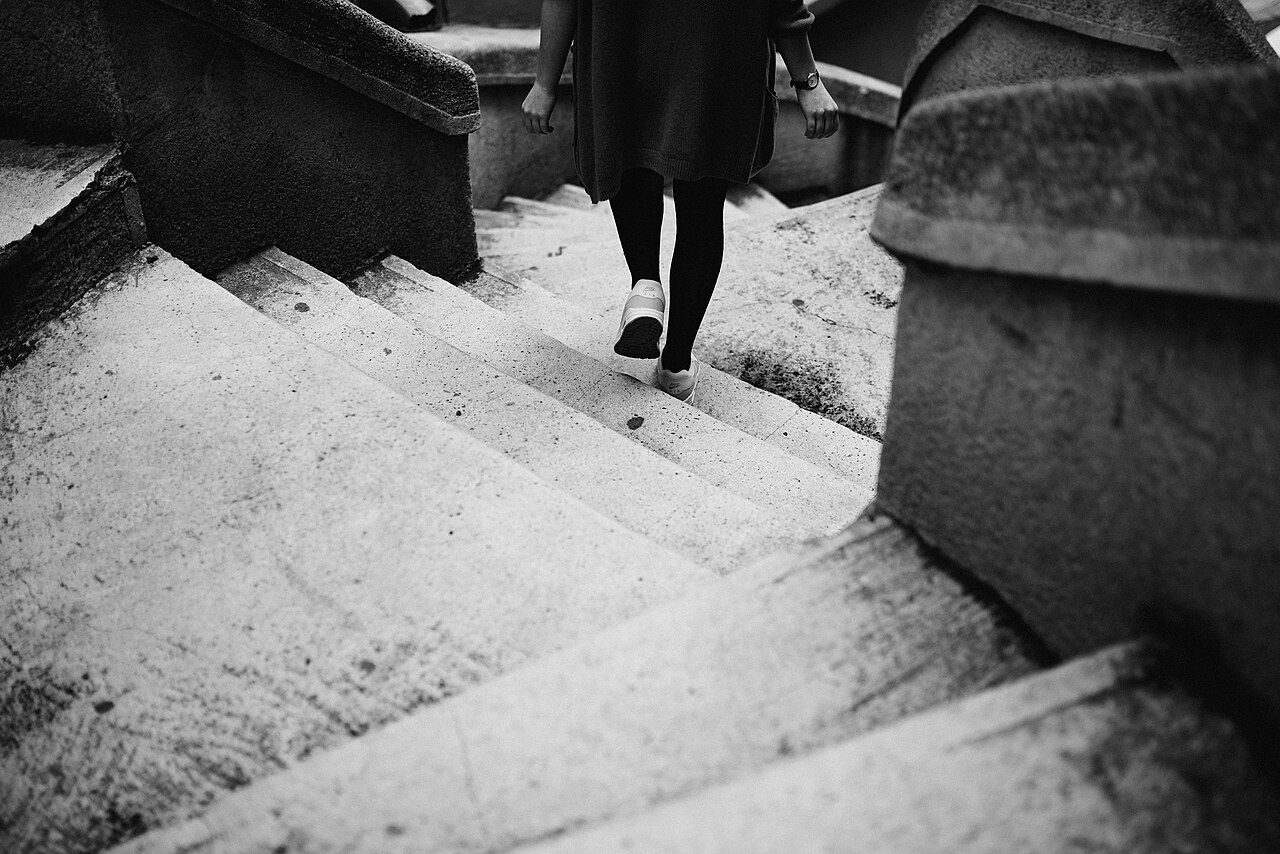 白黒写真。石の階段を、スニーカーの人が歩いている。足もとと階段だけが写っている。
